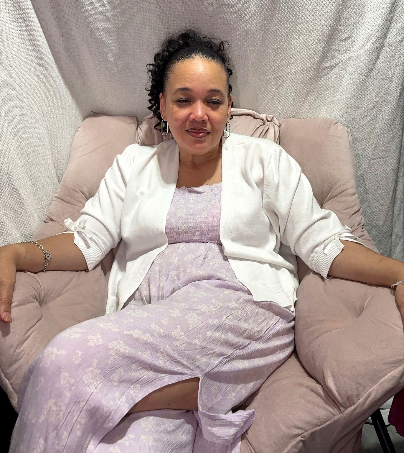 Sayyida Victoria Hillard seated in a cushioned chair, wearing a white cardigan over a lavender dress.